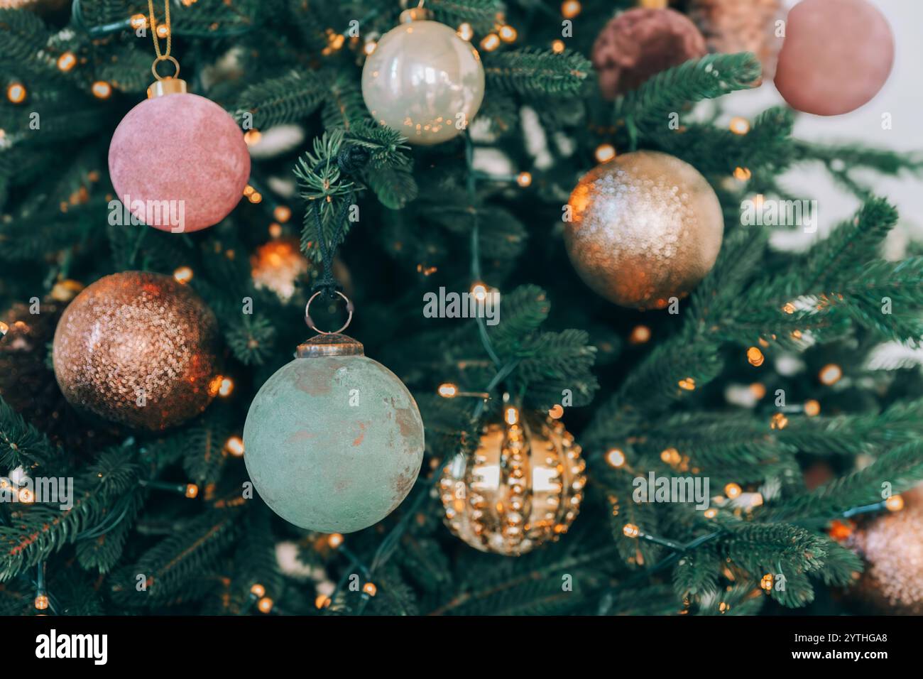 Wunderschön dekorierter Weihnachtsbaum mit verschiedenen Ornamenten in Rosa-, Gold- und Grüntönen. Funkelnde Lichter im Hintergrund unterstreichen festliche atmos Stockfoto