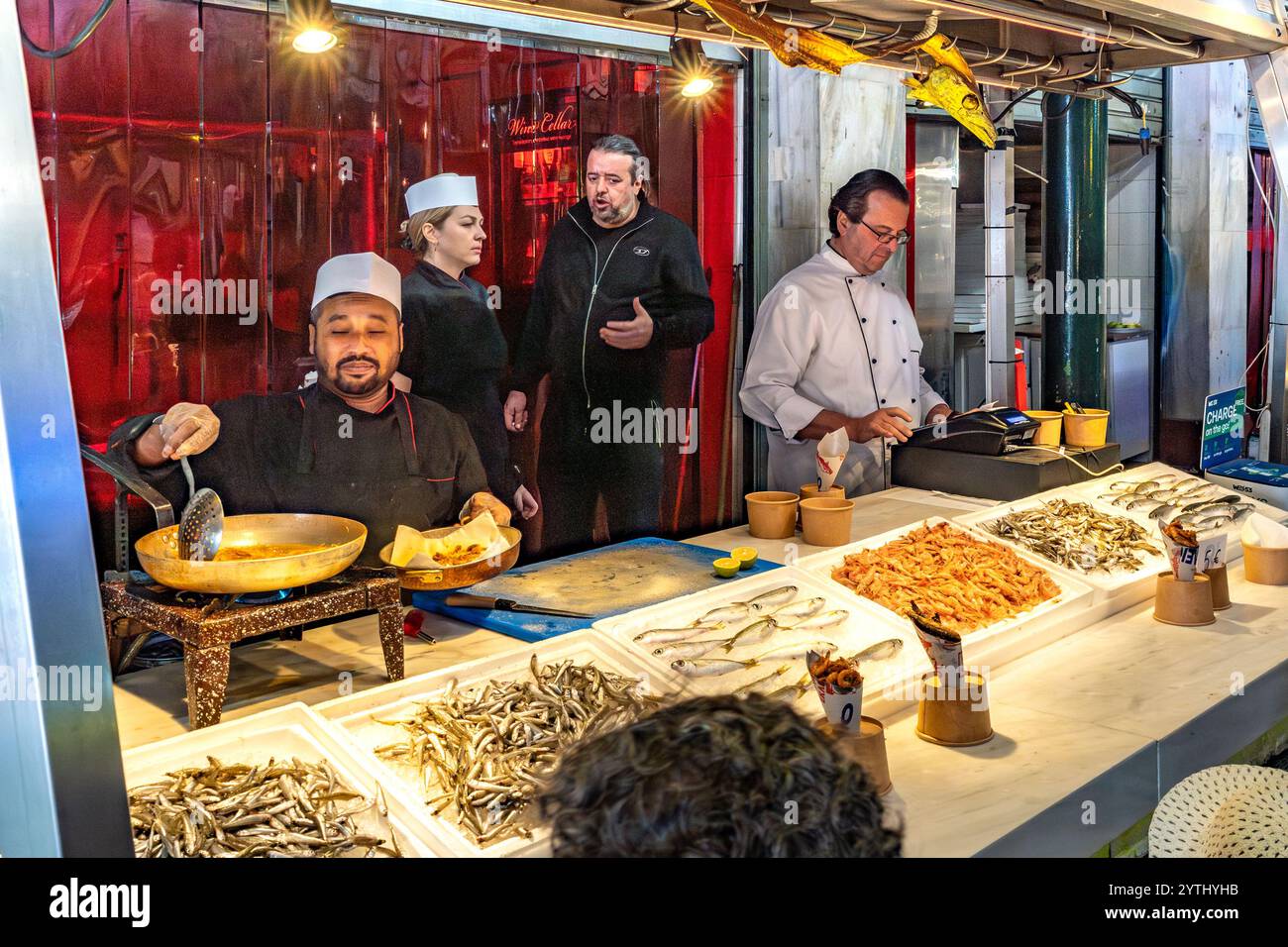 Athen, Attika - GR - 25. Okt. 2024 auf dem Varvakios Central Market frittieren Köche frische Meeresfrüchte, umgeben von Fisch und Garnelen, während die Einheimischen mich engagieren Stockfoto
