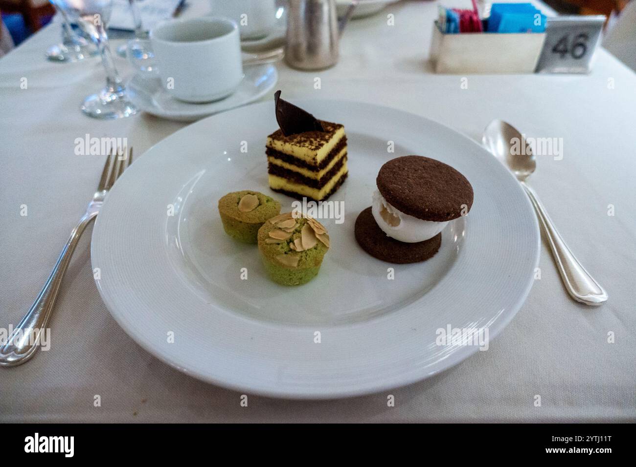 Ein überdachtes Desserttrio mit mehrschichtigem Kuchen mit Schokoladengarnitur, zwei gebackenen Gebäckstücken mit grüner Mandelplatte und einem Eissandwich mit Schokoladenkeks Stockfoto