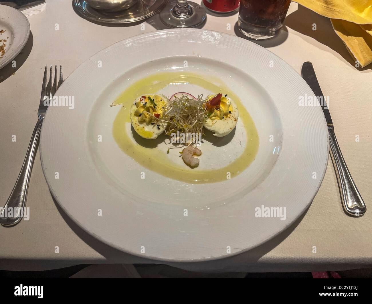 Eine raffinierte Präsentation von Eiern mit Meeresfrüchten, garniert mit Sprossen, essbaren Blumen und einem Spritzer Olivenöl, die cremige Texturen und das Meer vermischen Stockfoto