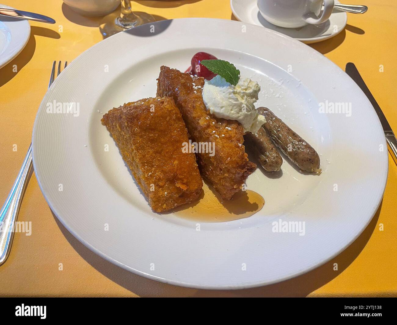 Ein überdachtes Frühstück mit knusprigem französischem Toast mit Schlagsahne und Minze, begleitet von Würstchen, Sirup und einer Seite Strohhalm Stockfoto