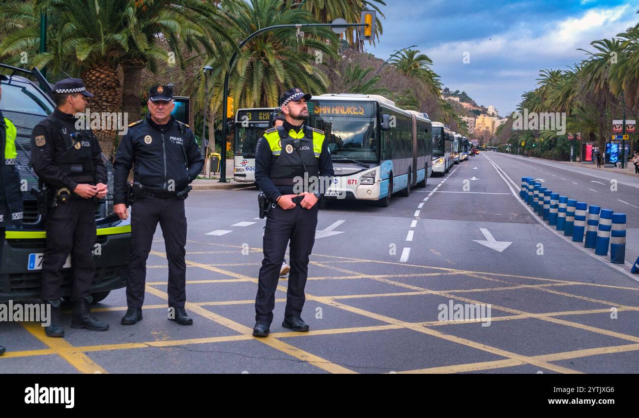 Die europäischen Polizisten verwalten den Verkehr zwischen geparkten Bussen und Sun Andreas auf einer palmengesäumten Straße, potenzielle Großveranstaltungen in bedecktem Licht. Stockfoto