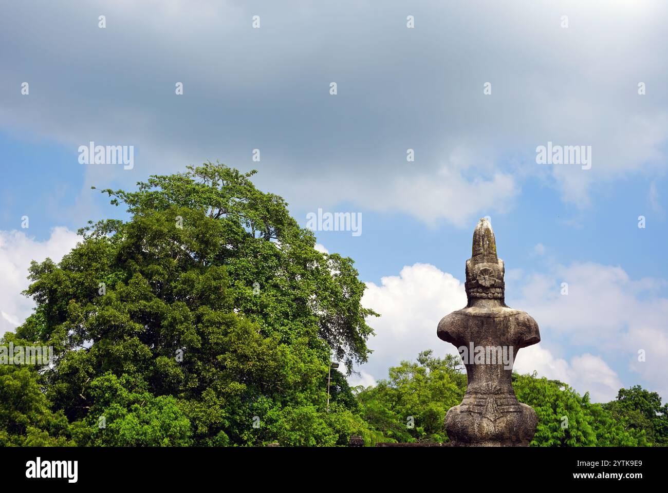 Antike Steinstatue mit Blick auf üppiges Grün unter einem ruhigen Himmel, die die Harmonie des kulturellen Erbes und der natürlichen Schönheit in Polonnaruwa einfängt. Stockfoto