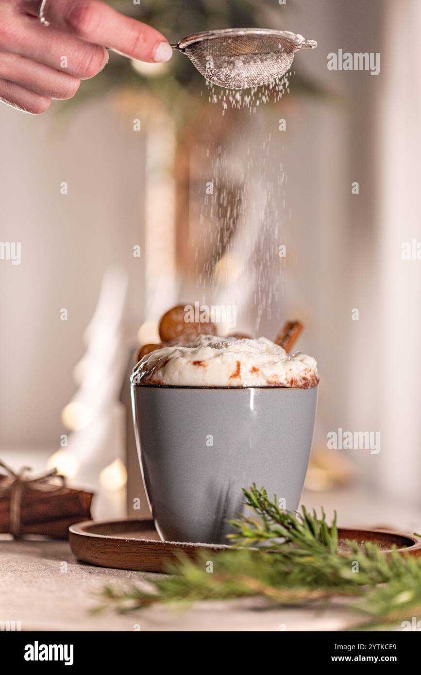 Koch streut Puderzucker auf köstliche heisse Weihnachtsschokolade mit verschwommenem festlichem Hintergrund Stockfoto