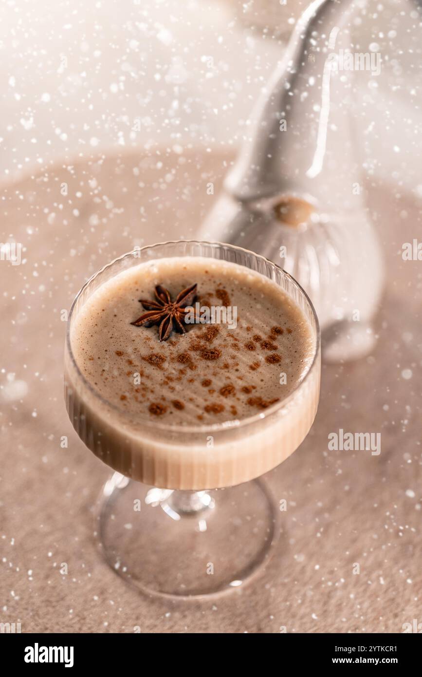 Eierlikör-Cocktail, dekoriert mit Sternanis und Zimtpulver, fallender Schneeeffekt Stockfoto