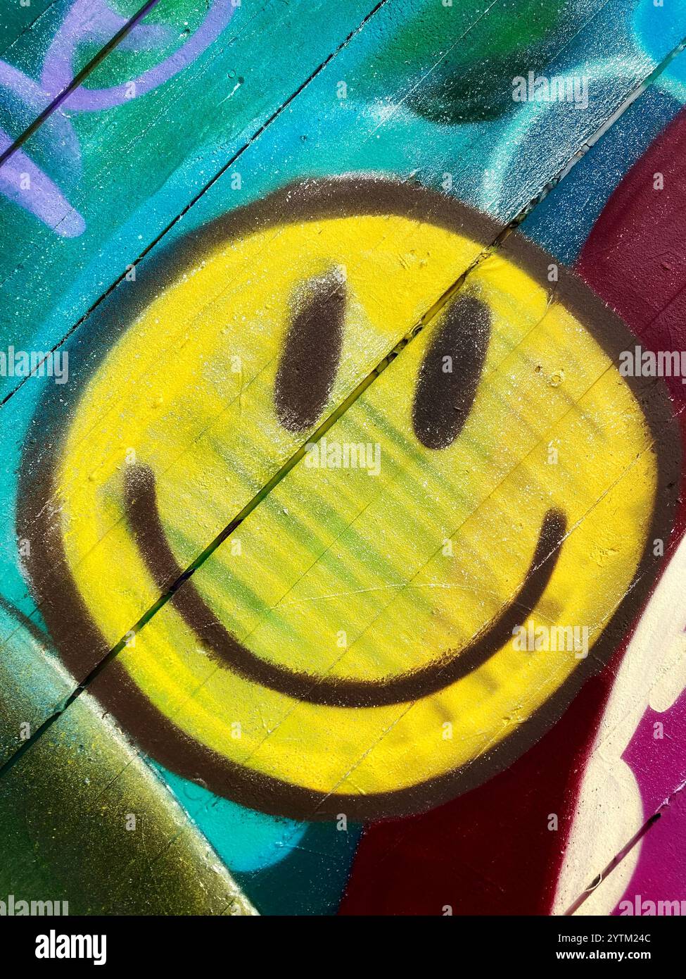 Ein gesprühtes Smiley-Emoji an einer Holzwand - Smartphone-aufgenommenes Stockfoto