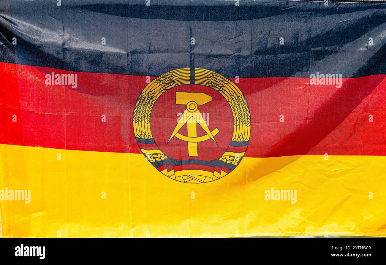 Hüntwangen, Schweiz, 24. August 2024: Die Flagge der DDR mit Hammer, Kompass und Weizenkranz in Schwarz, Rot und Gold. Stockfoto