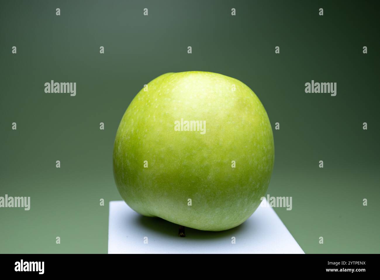 , Deutschland, 07.12.2024, ein frischer, grüner Apfel auf einer weißen Erhöhung vor einem grünen Hintergrund, symbolisiert gesunde Ernährung und natü Stockfoto