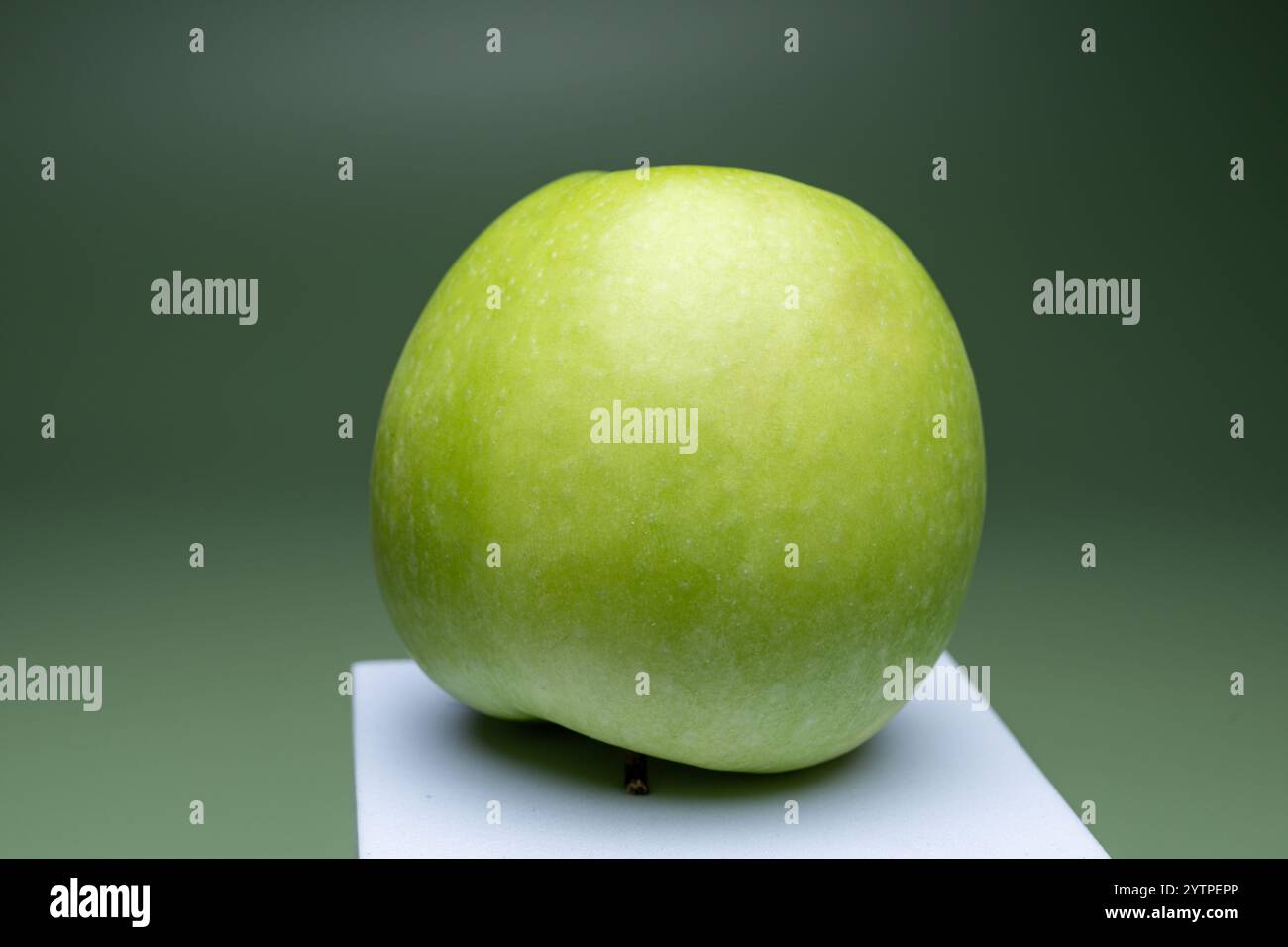 , Deutschland, 07.12.2024, ein frischer, grüner Apfel auf einer weißen Erhöhung vor einem grünen Hintergrund, symbolisiert gesunde Ernährung und natü Stockfoto