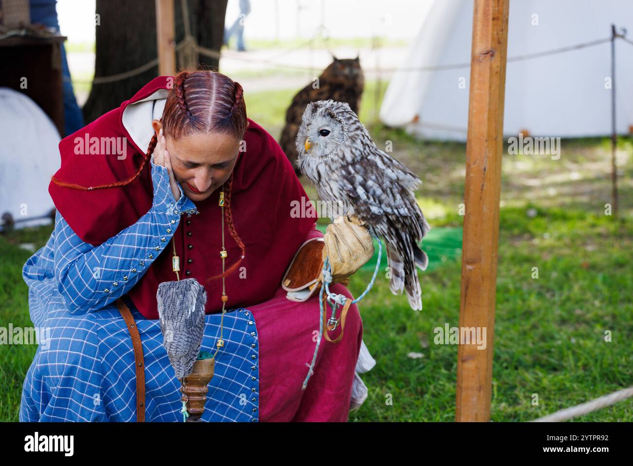 Mantova, Italien – 15. September 2024: Eine Frau in mittelalterlichen Gewändern hockt sich mit einer Eule am Arm und lauscht während einer historischen reena ihrem sanften Rauschen Stockfoto