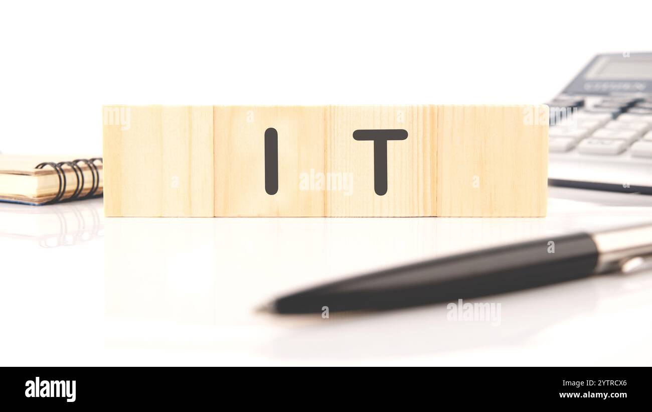 Informationstechnologie. ES ist auf Holzwürfeln geschrieben, in einer Komposition mit Taschenrechner, Stift, Notizbuch auf weißem Hintergrund. Stockfoto