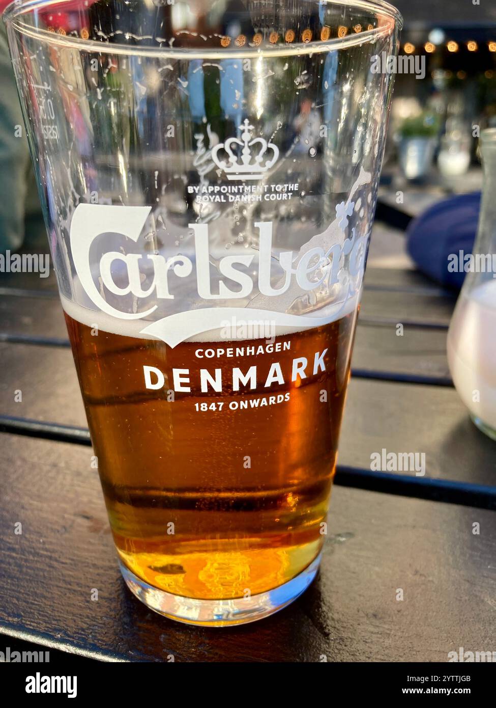 Ein halbes getrunkenes Glas Carlsberg Bier auf einem Tisch im Außenbereich eines Pubs in Kopenhagen, Dänemark Stockfoto