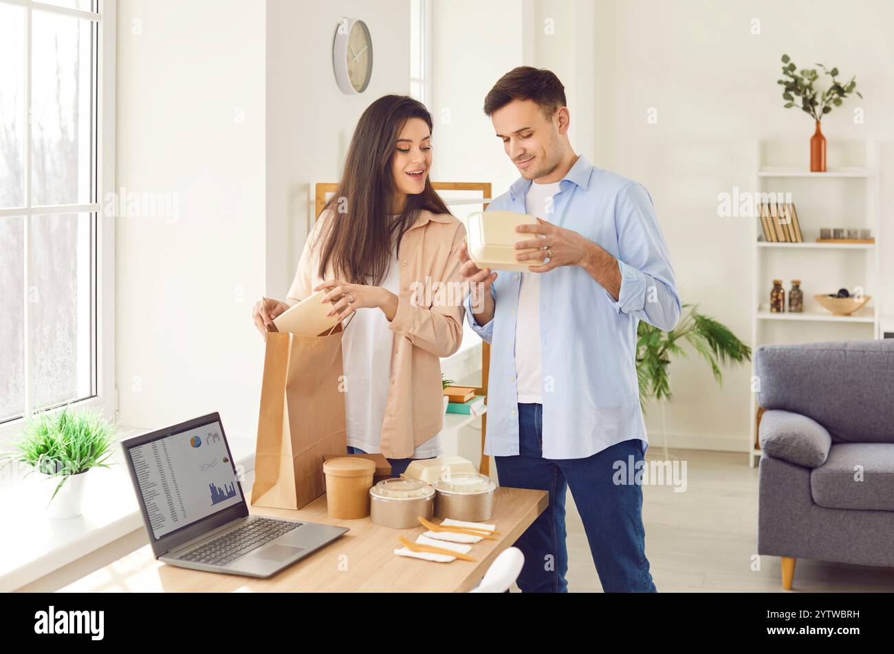 Junger glücklicher Mann und Frau, die Lebensmittelverpackungen mit Lebensmitteln aus Pappkartons aus Online-Bestellung auspacken. Stockfoto