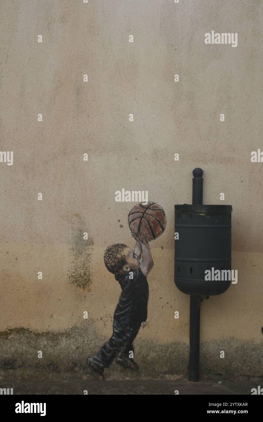 Banksy-Stil Graffiti, Junge mit Korbball, der in einen Mülleimer taucht Stockfoto