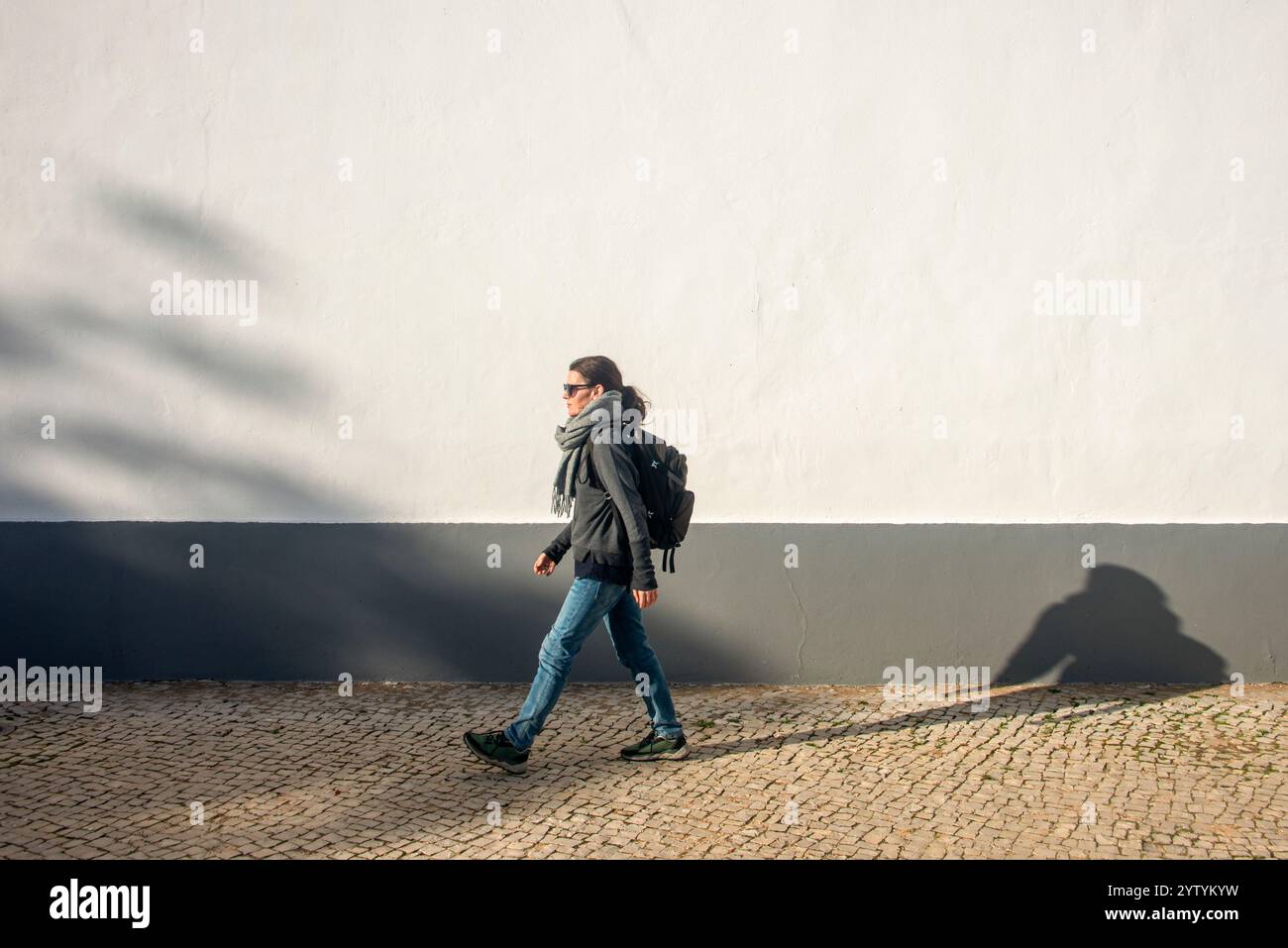 Frau mit Rucksack, die an einer weißen Wand vorbeigeht, Sport. Stockfoto