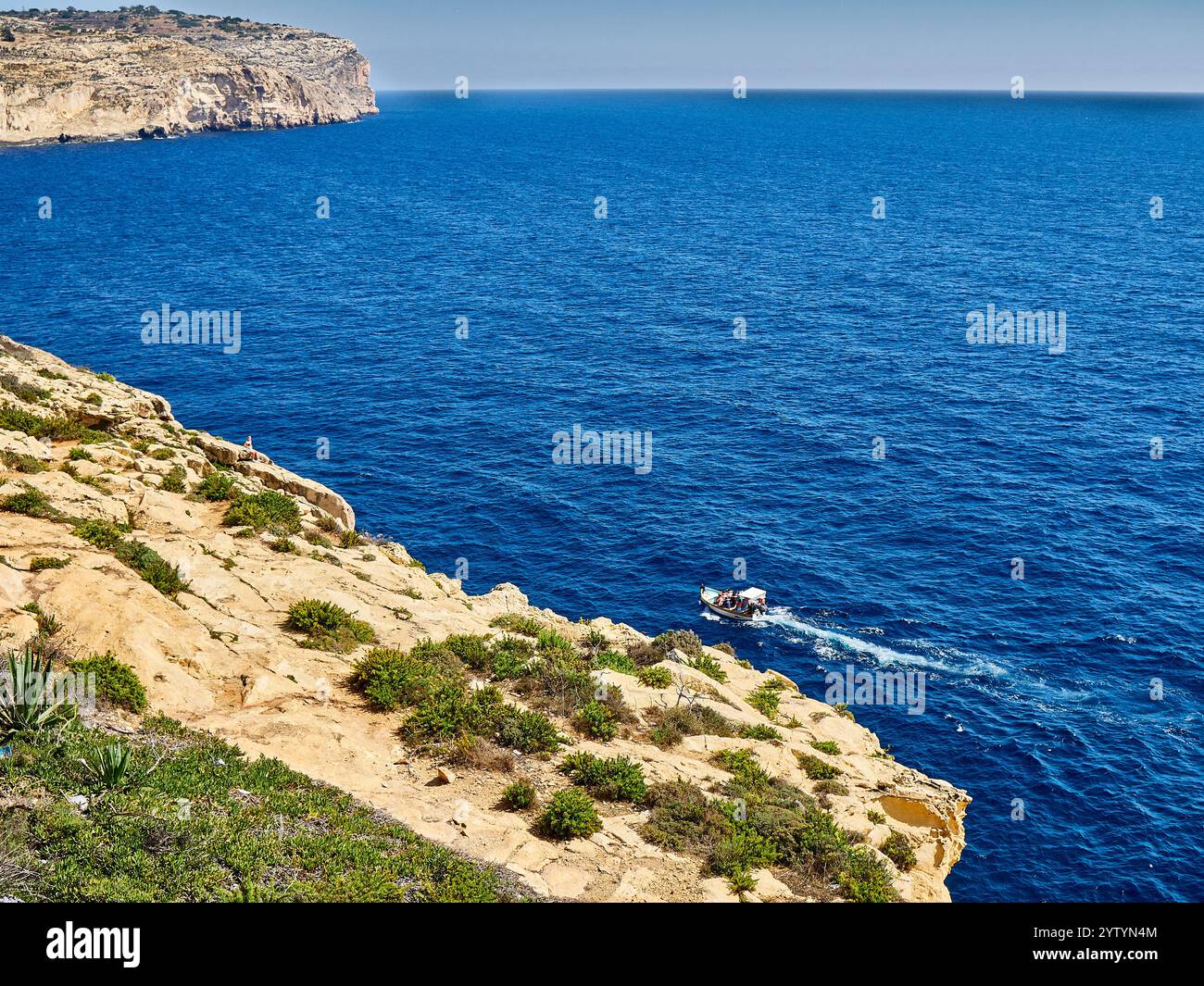 Ein Blick auf die felsige Küste und das Mittelmeer, auf dem ein Boot segelt, Malta Stockfoto