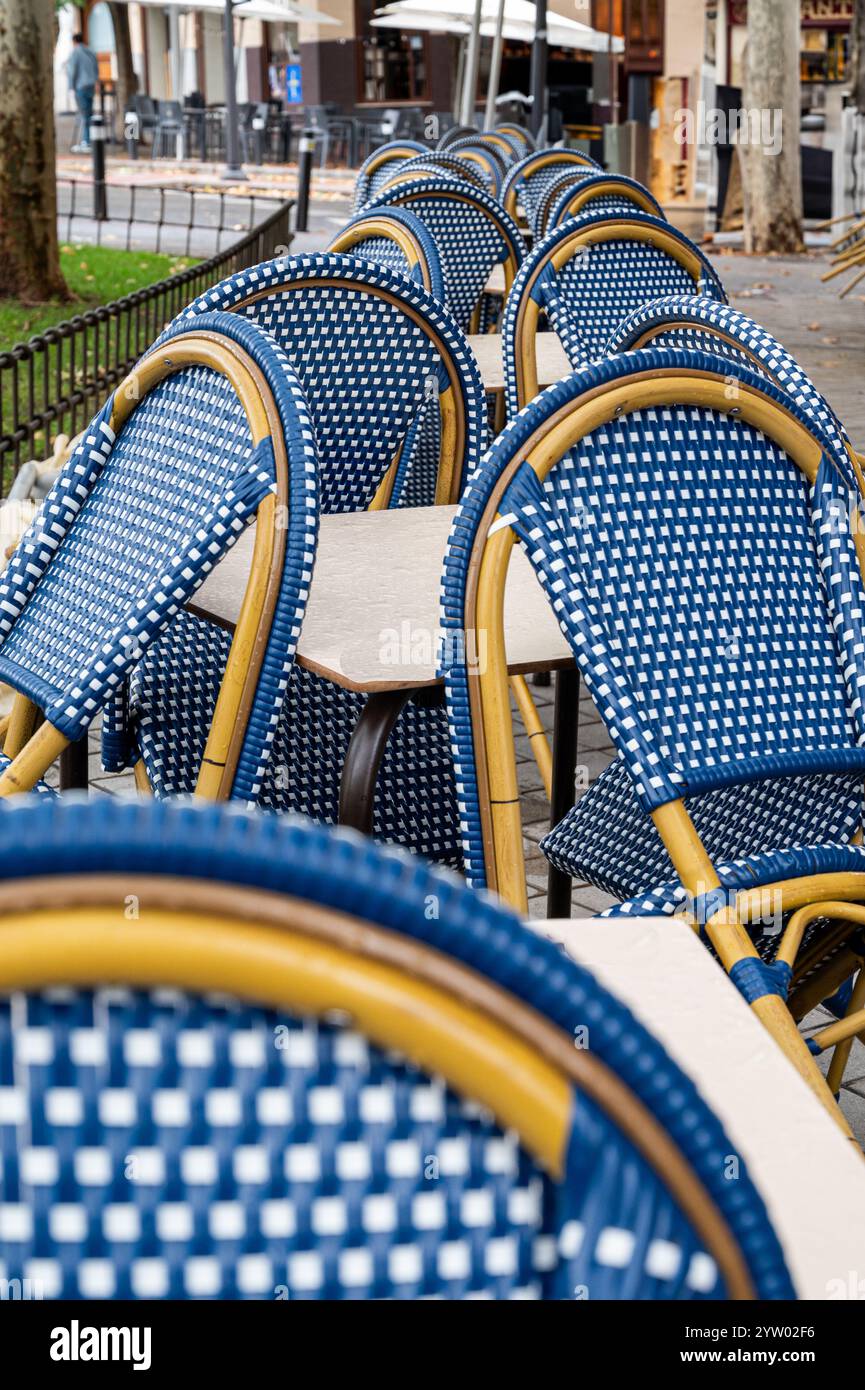 Eine Reihe blauer und gelber Stühle steht auf einem Bürgersteig leer. Die Stühle sind in einer Reihe angeordnet, einige davon zur Straße hin Stockfoto