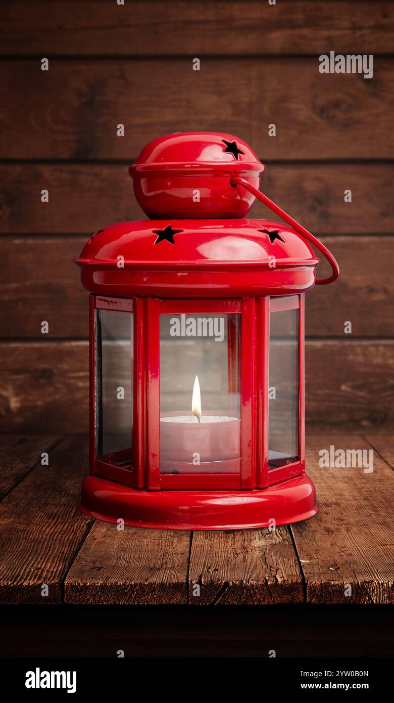 Rote Laterne mit einer glühenden Flamme auf einem rustikalen Holztisch, die vor dem alten Innenraum einer Hütte steht und eine romantische Weihnachtsatmosphäre weckt Stockfoto