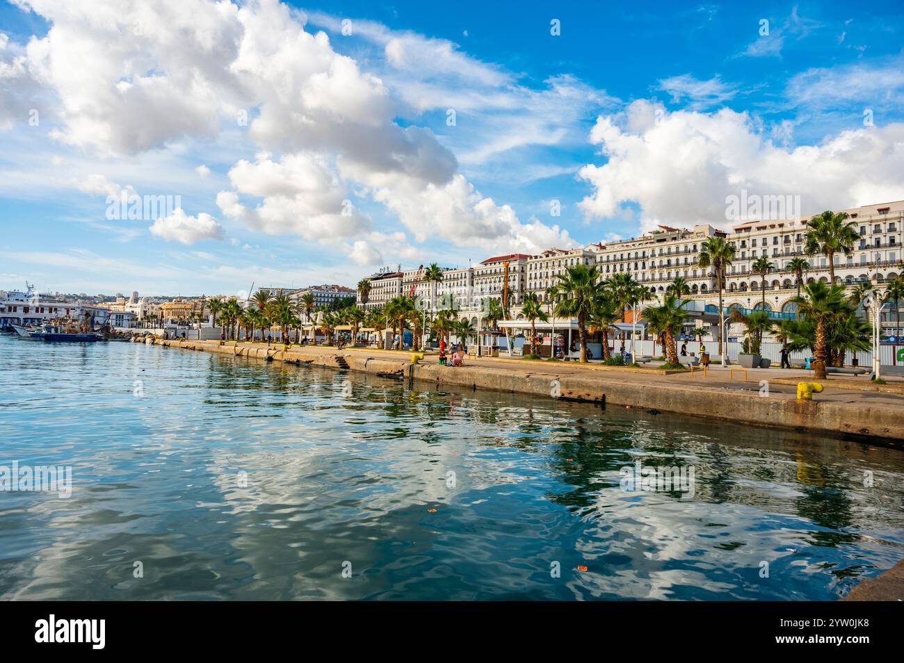 Vue Panorama sur le Front de mer d'Alger, avec des palmiers, des bâtiments koloniaux et un ciel bleu partiellement nuageux Stockfoto