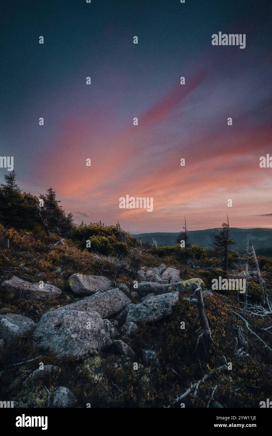 Ein atemberaubender Sonnenuntergang entfaltet sich über einem malerischen felsigen Hügel mit wunderschönen Bäumen, die die Szene im Vordergrund umrahmen Stockfoto