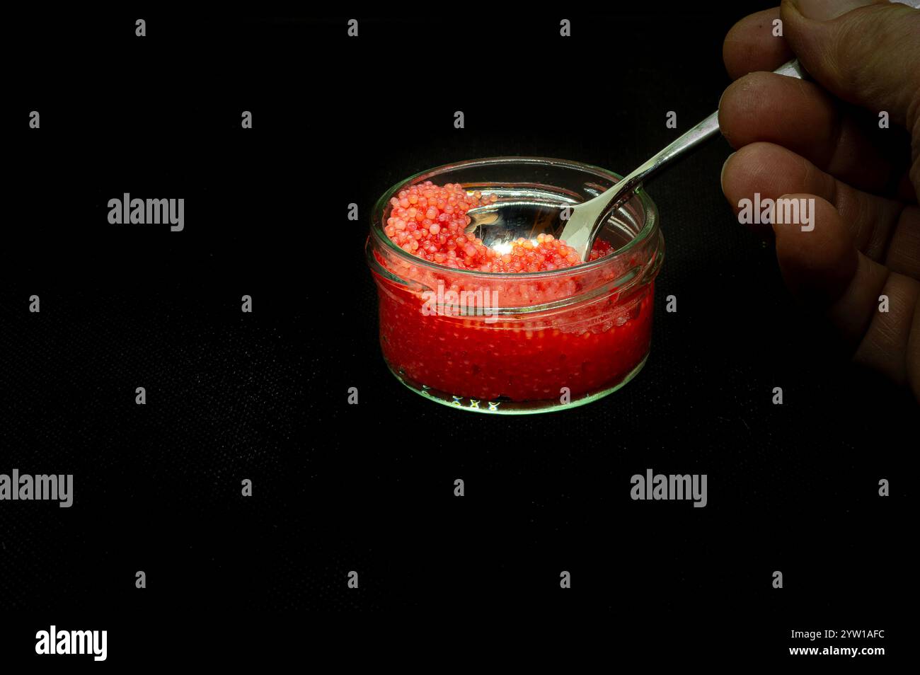 Glasgefäß mit rotem Lumpfischrogen und einer Hand, die einen Löffel hält Stockfoto