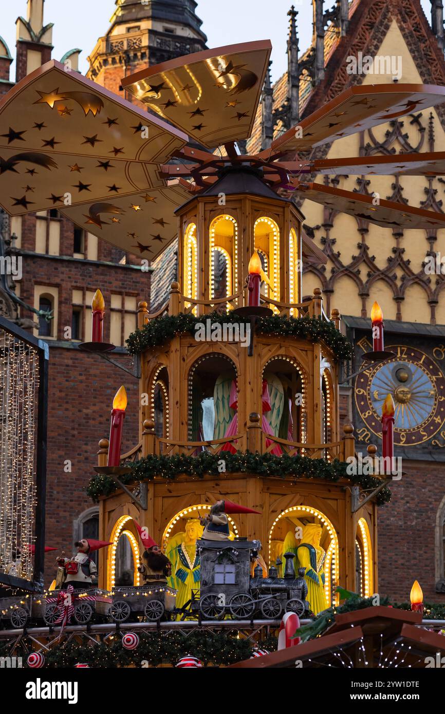 Festliche beleuchtete Weihnachtspyramide mit farbenfrohen Engelsfiguren und dekorativer Bahn auf dem Weihnachtsmarkt vor historischer gotischer Architektur Stockfoto