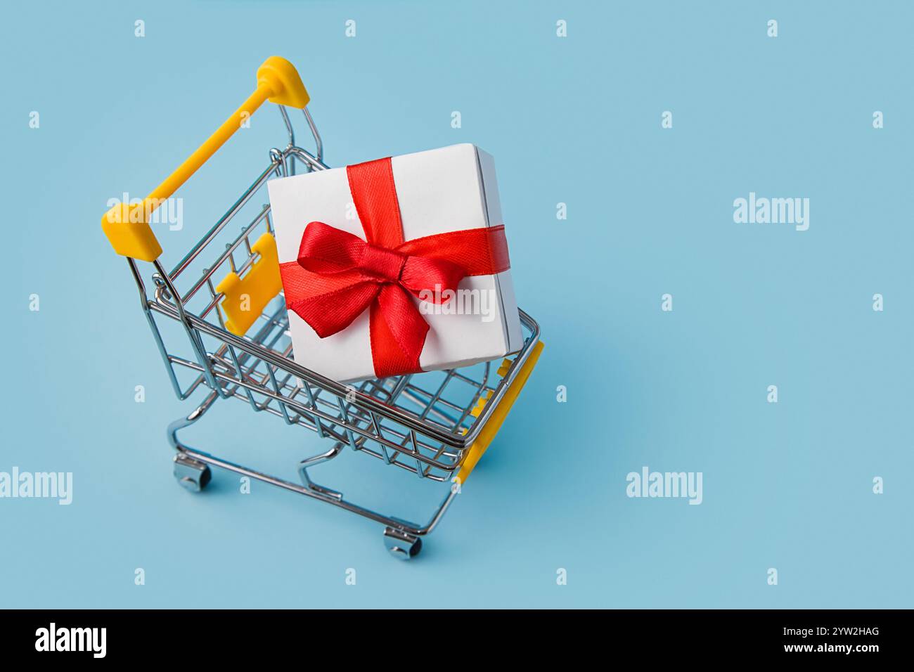 Warenkorb mit großer Geschenkbox auf blauem Hintergrund. Weihnachtseinkaufskonzept. Online-Shopping-Konzept Stockfoto