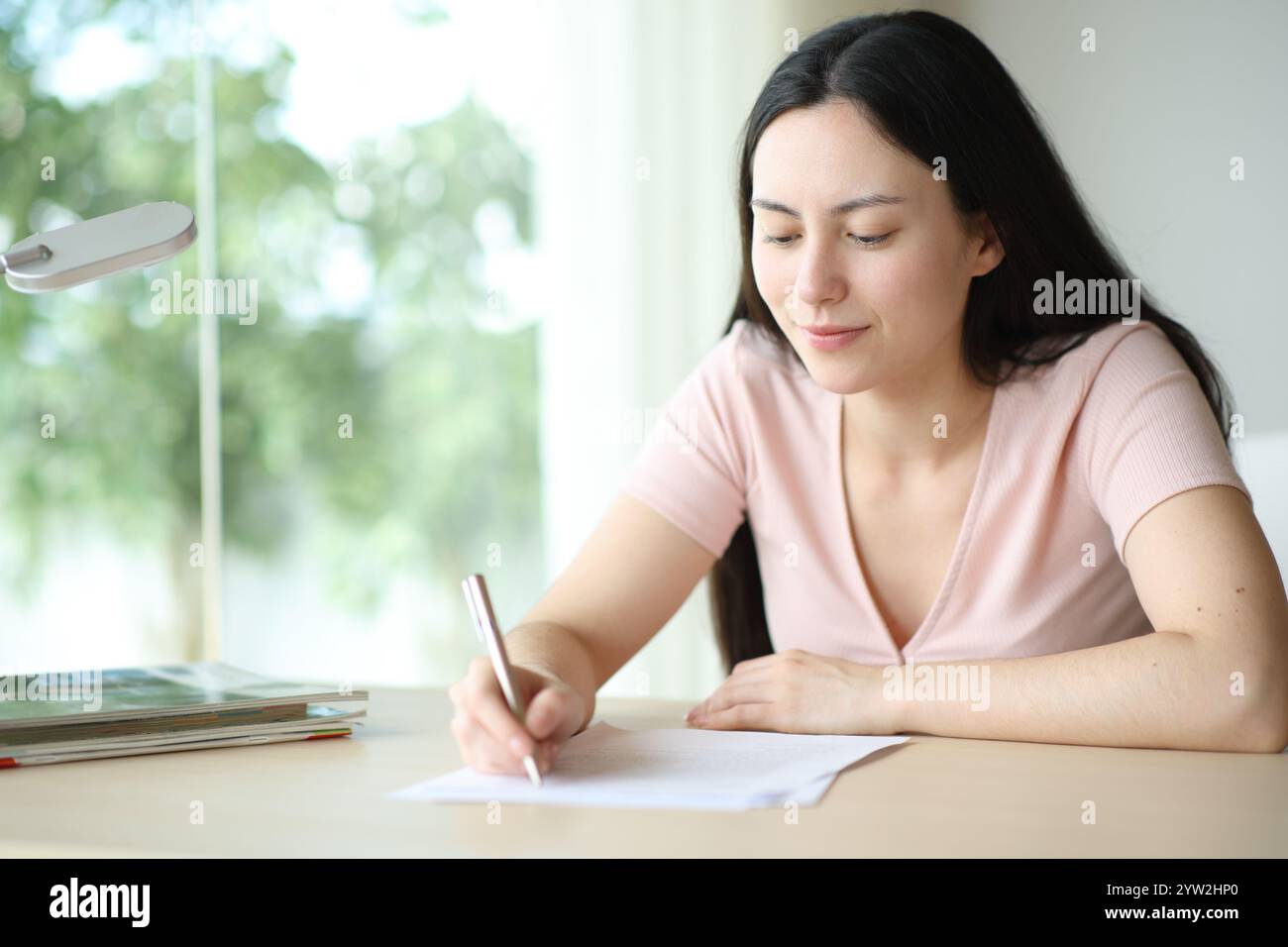 Asiatische Frau unterschreibt einen Vertrag oder füllt ein Formular an einem Schreibtisch zu Hause aus Stockfoto