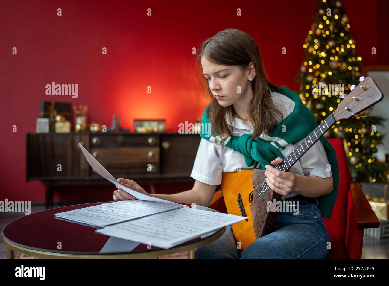 Eine fokussierte Frau studiert Balalaika-Lied, liest Noten. Vorbereitung der Weihnachtsfeier, Hausaufgaben Stockfoto