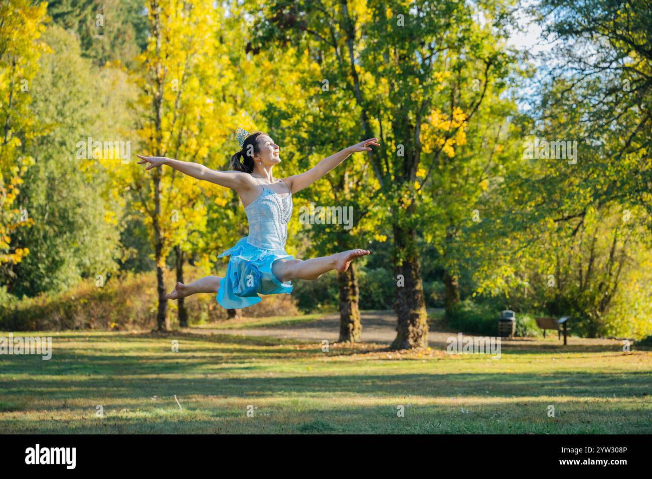 Fröhliche Frau tanzt in einem sonnendurchfluteten Park mit Herbstbäumen im Hintergrund. Stockfoto
