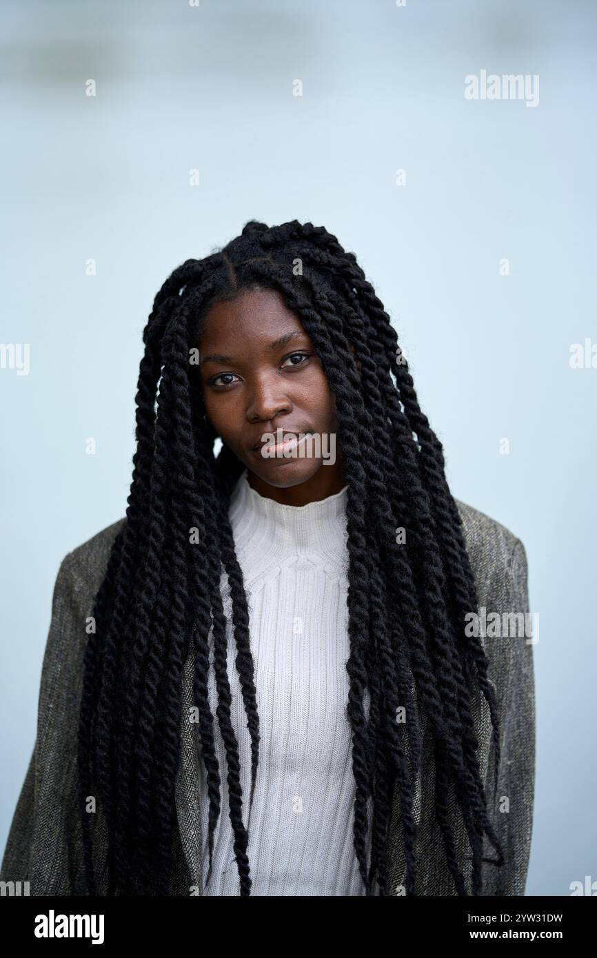 Porträt einer jungen Frau mit geflochtenen Haaren in weißem Pullover und grauem Blazer auf weichem blauem Hintergrund, Brandenburg, Deutschland Stockfoto