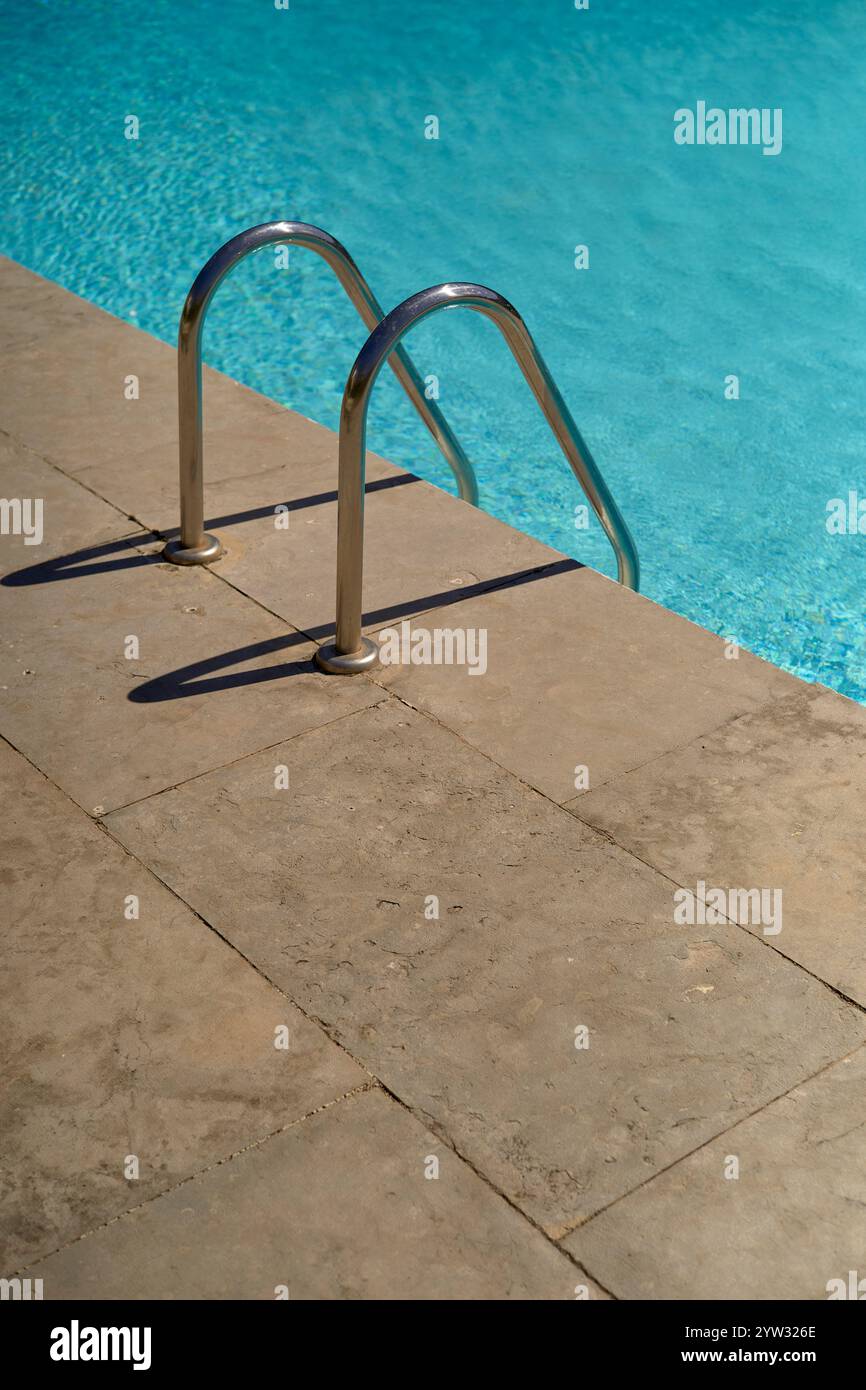 Die Schwimmbadleiter aus Edelstahl führt an einem sonnigen Tag in klares blaues Schwimmbadwasser, Portugal Stockfoto