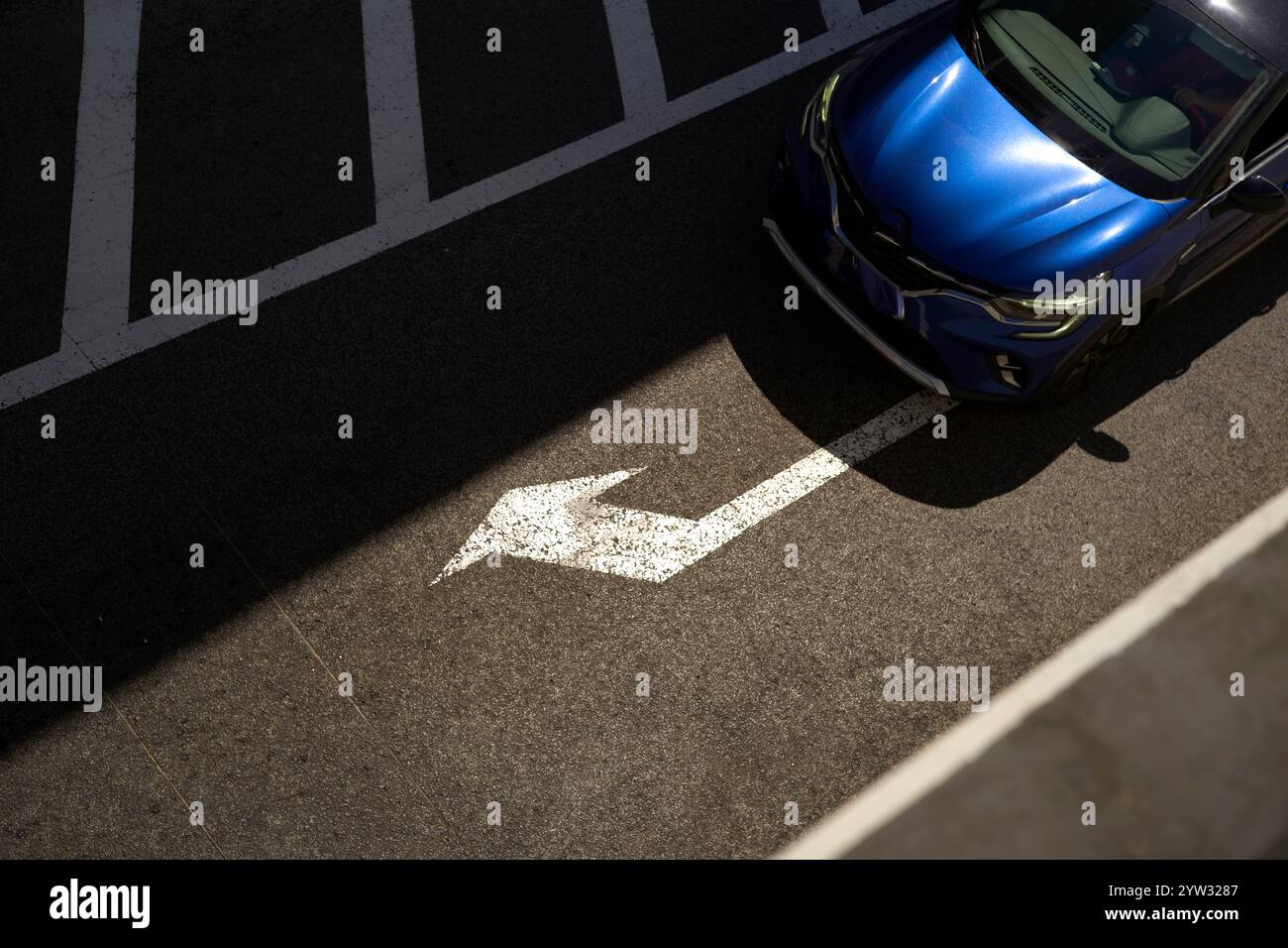 Blaues Auto parkt neben einem weißen Pfeil auf einer Asphaltoberfläche mit Parkplatzlinien, Portugal Stockfoto