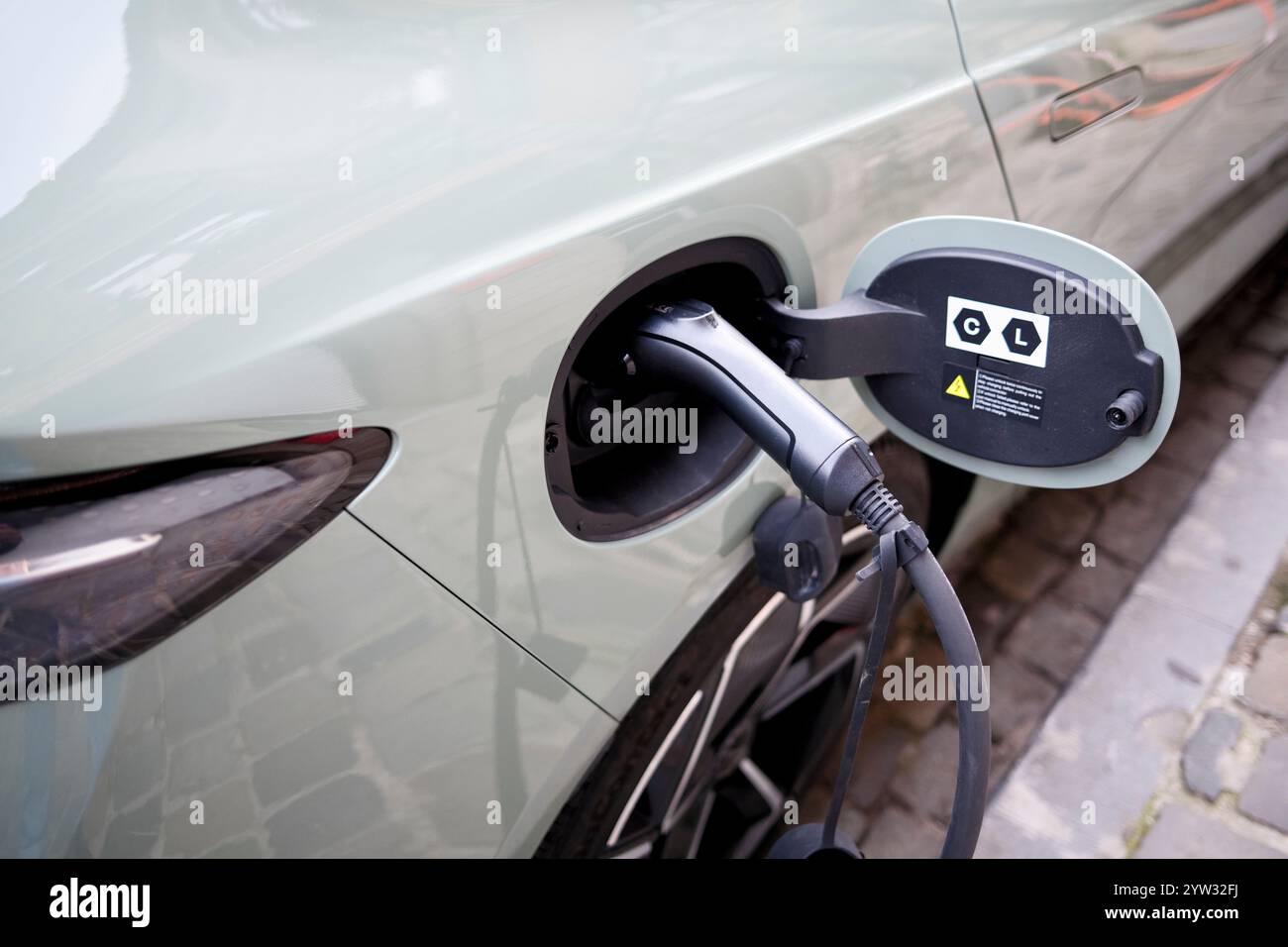 Elektroauto angeschlossen und an einer Straßenladestation mit Schwerpunkt auf Netzkabel und Ladeanschluss aufgeladen. Stockfoto