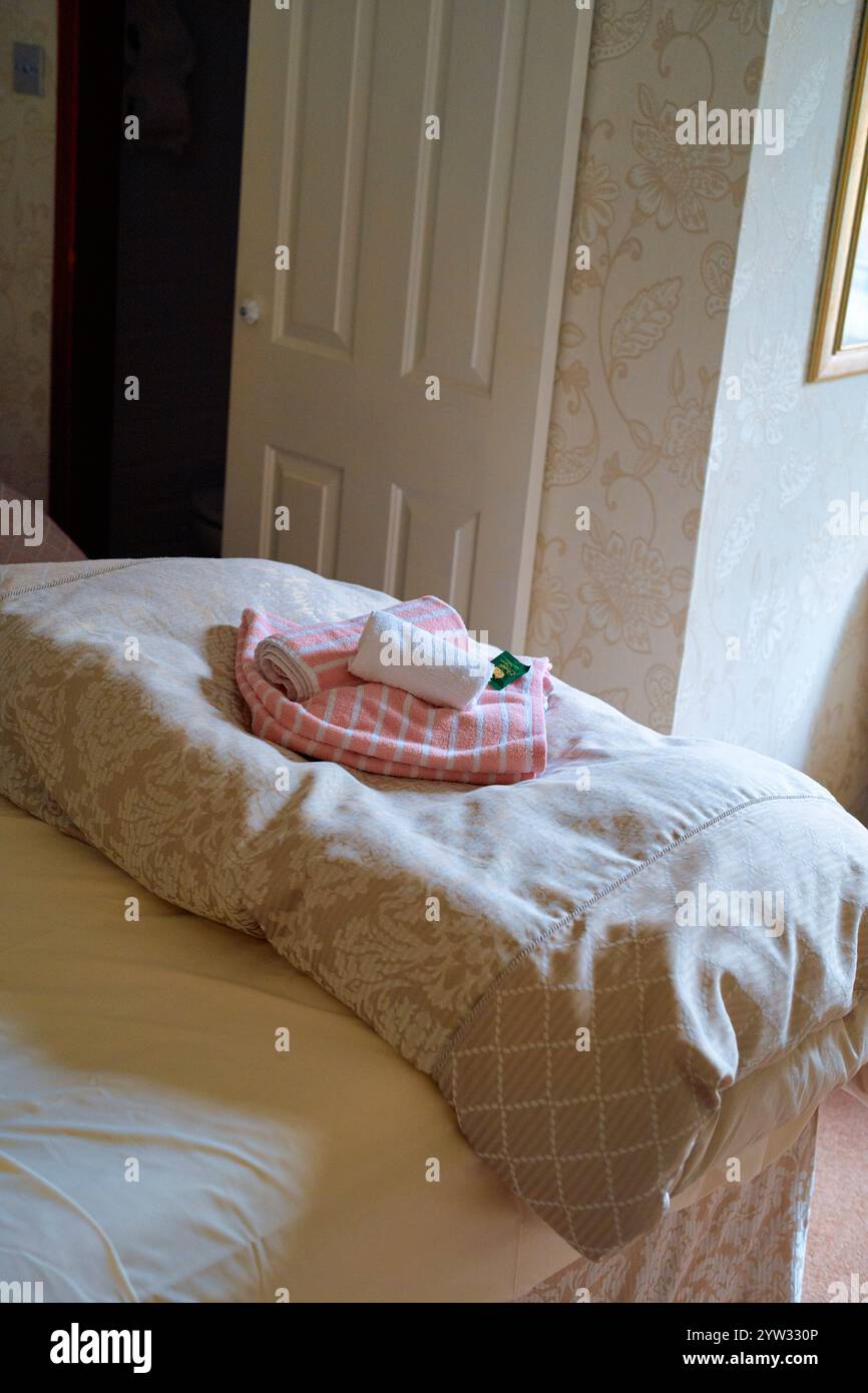 Ein ordentlich gefertigtes Bett mit einem pinkfarbenen Handtuch-Schwan-Dekor oben, in einem Zimmer mit Vintage-Tapeten und einer geschlossenen weißen Tür, Schottland Stockfoto