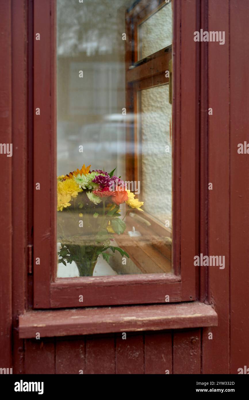 Ein bunter Blumenstrauß in einer Vase auf einer Fensterbank hinter einem Holzfenster, Schottland Stockfoto