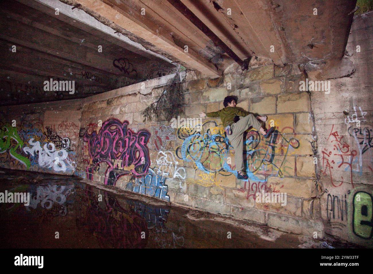 Junge Kletterer Bouldern unter einer urbanen Brücke umgeben von Graffiti. Stockfoto