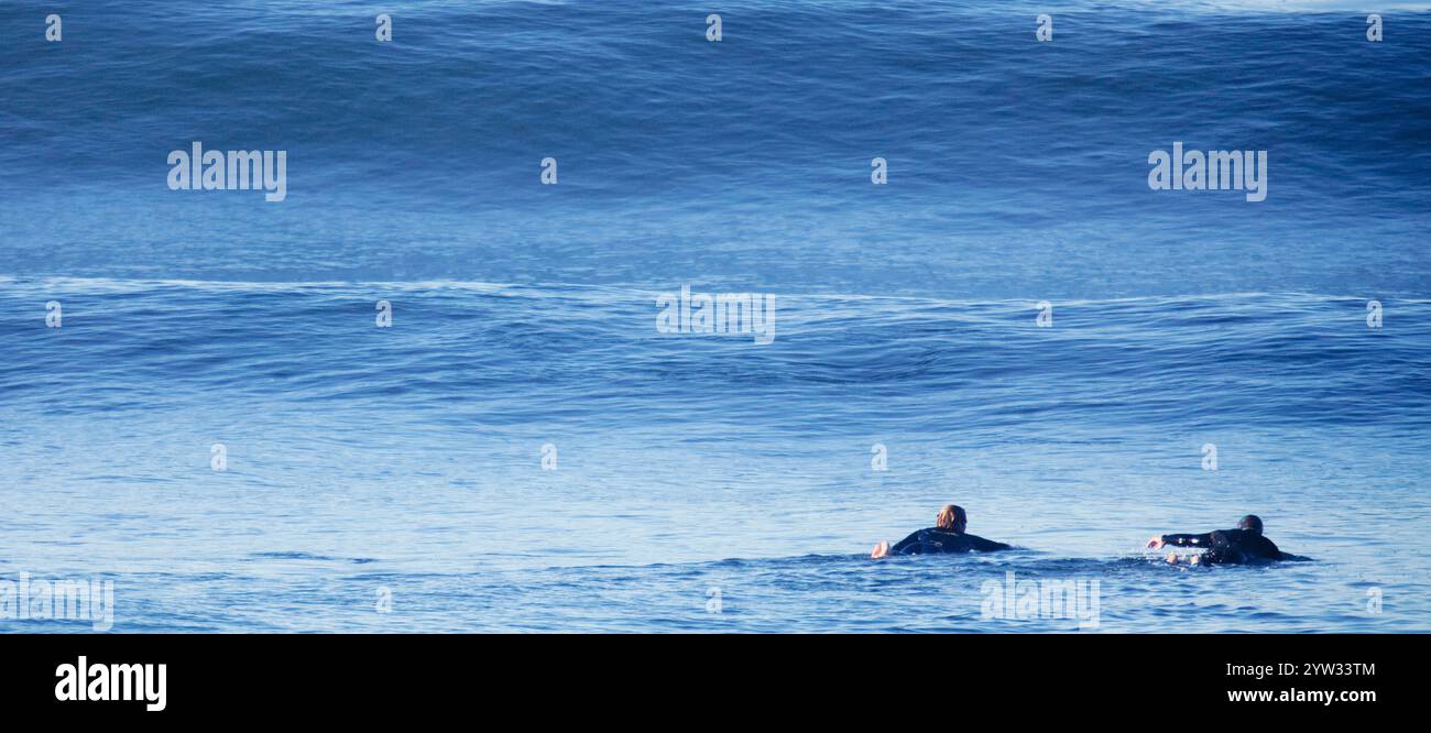 Zwei Surfer paddeln mit einer riesigen Welle im Hintergrund zur Besetzung. Stockfoto