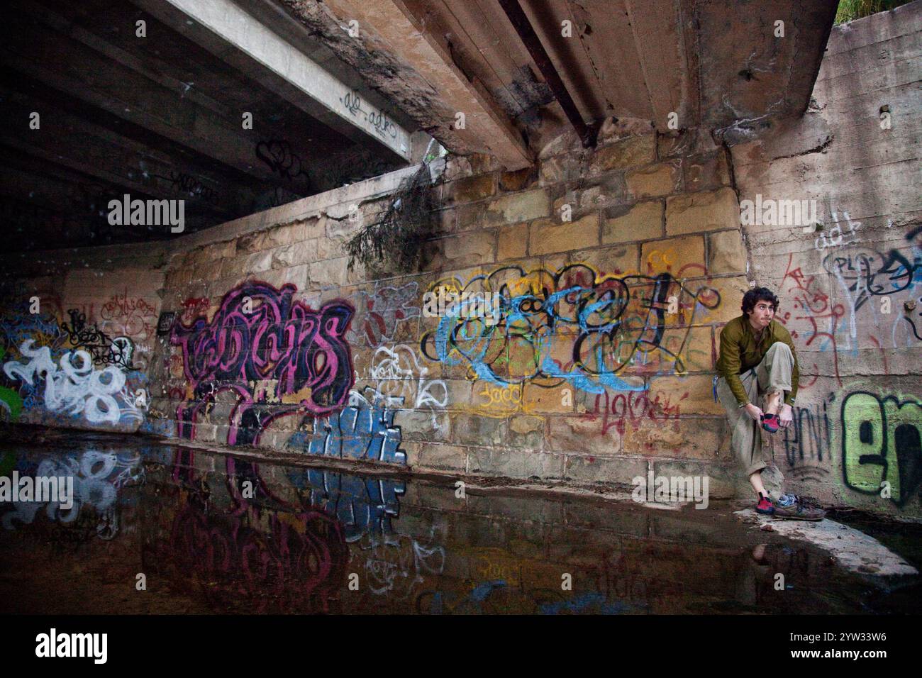 Junge Kletterer Bouldern unter einer urbanen Brücke umgeben von Graffiti. Stockfoto