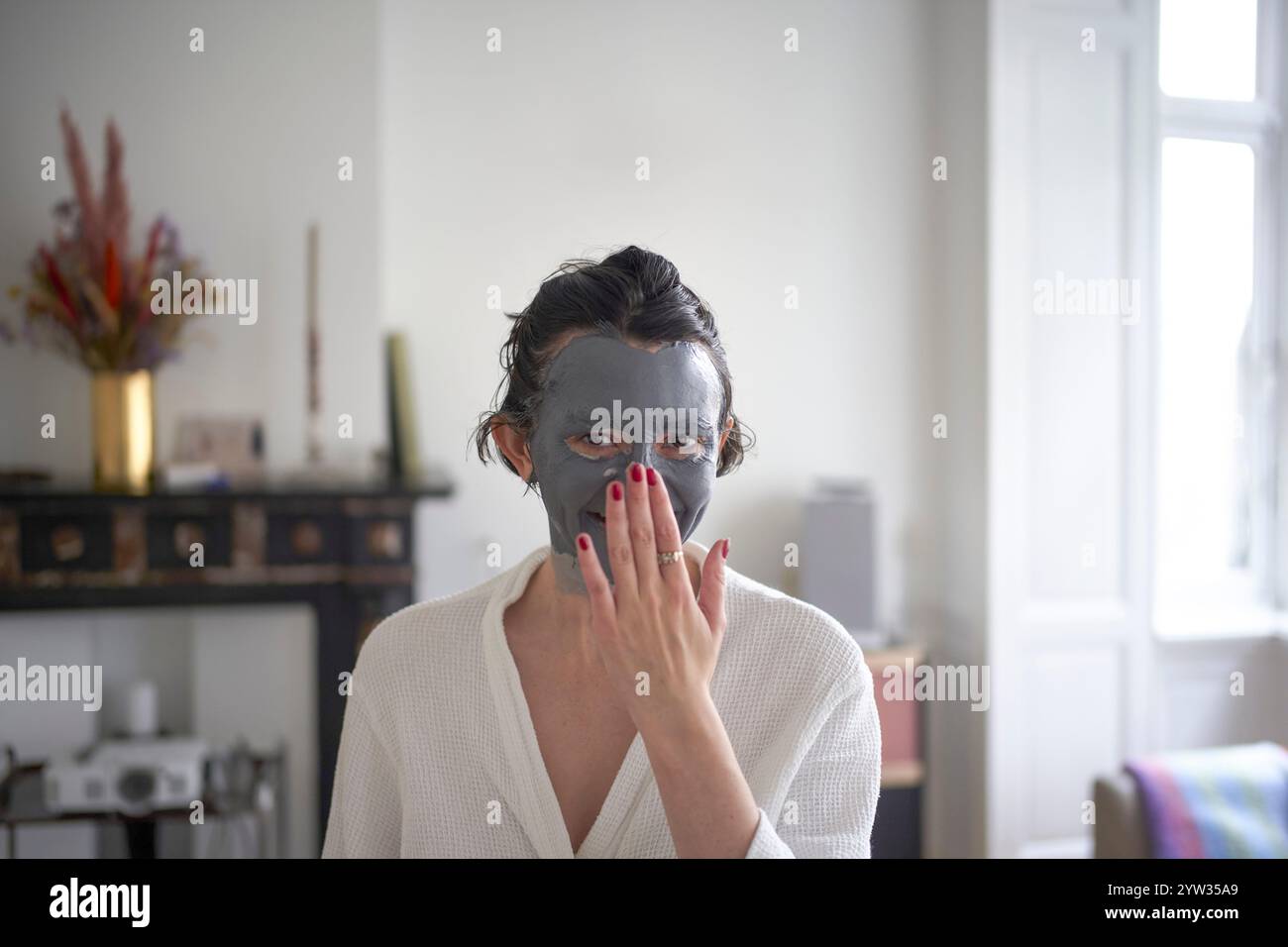 Eine junge Frau, die eine Gesichtsmaske trägt, blickt in einem hell beleuchteten Raum mit einer Hand in die Kamera. Stockfoto