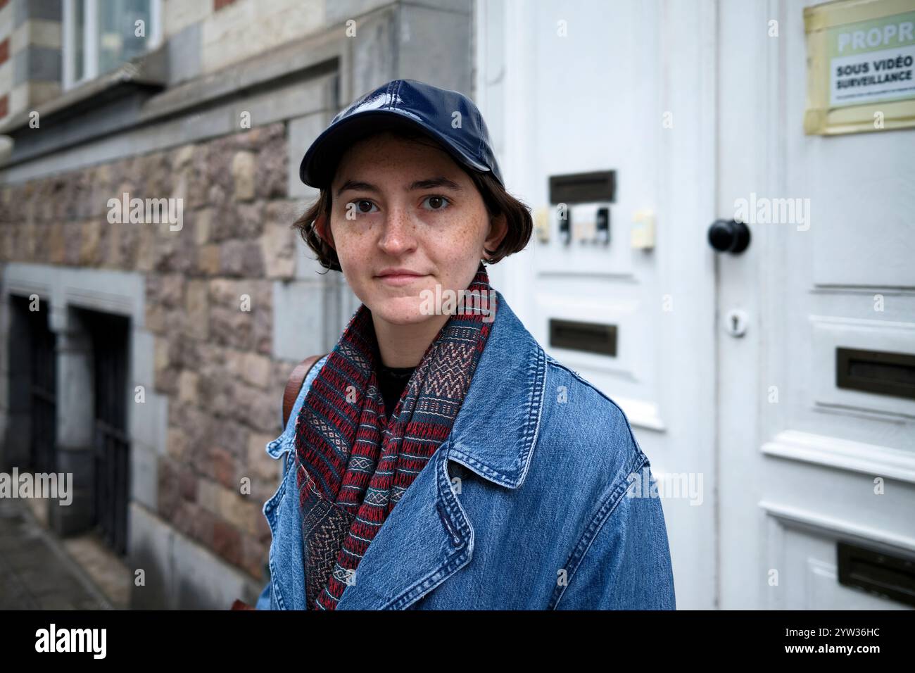 Frau in Jeansjacke und gemustertem Schal vor einem Steingebäude mit weißer Tür. Stockfoto