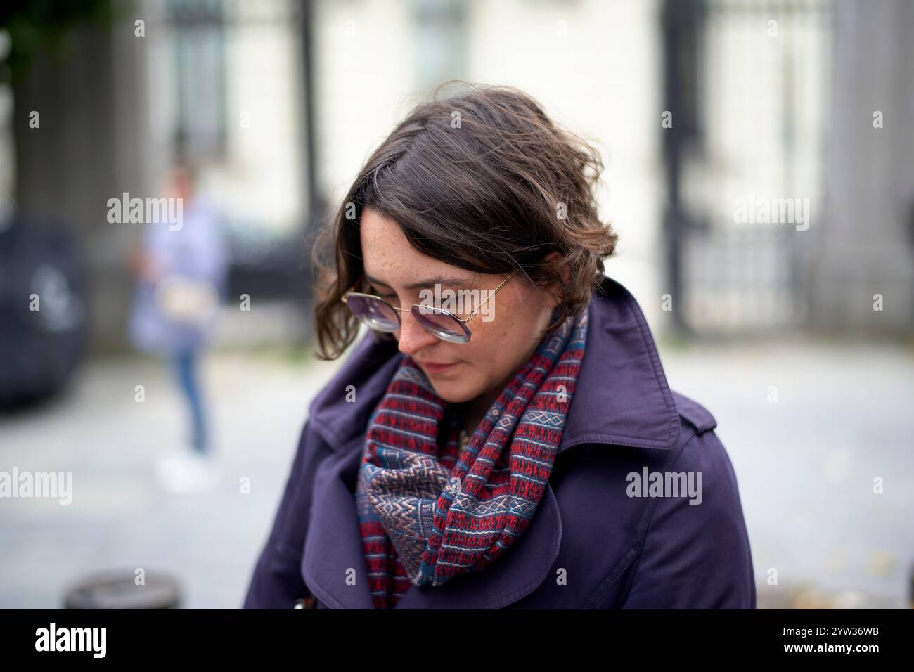 Eine Frau in einer lila Jacke mit einem mehrfarbigen Schal blickt nachdenklich auf eine Straße der Stadt. Stockfoto