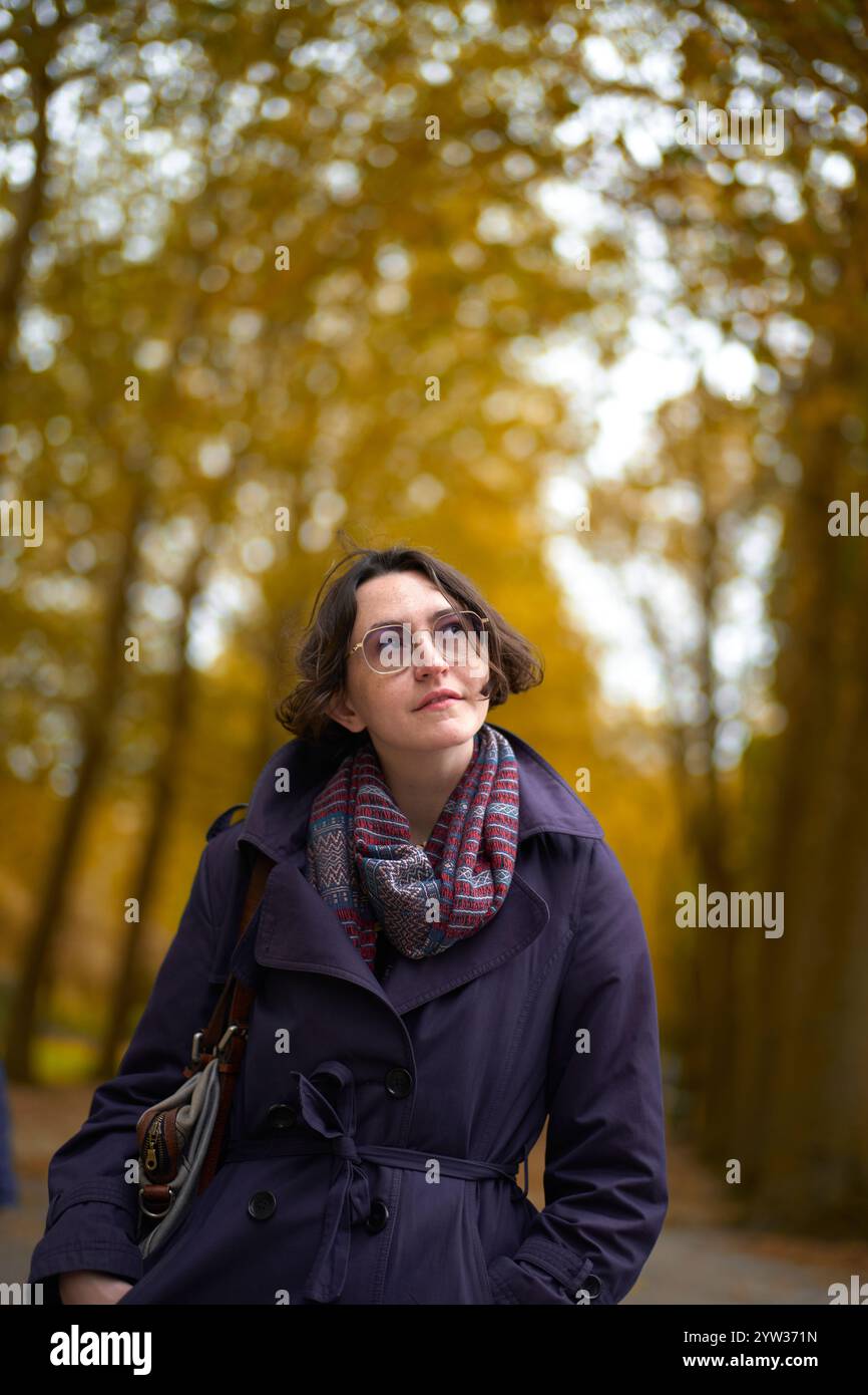 Nachdenkliche Frau in blauem Mantel und kariertem Schal in einem herbstlichen Park. Stockfoto