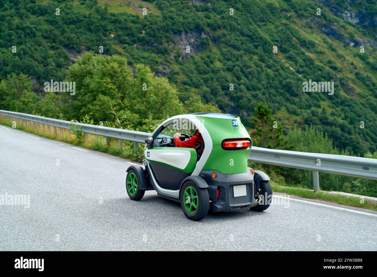 Umweltfreundliches kompaktes Elektroauto, das auf einer Bergstraße mit üppigem Grün im Hintergrund fährt, Geirangerfjord, Norwegen Stockfoto