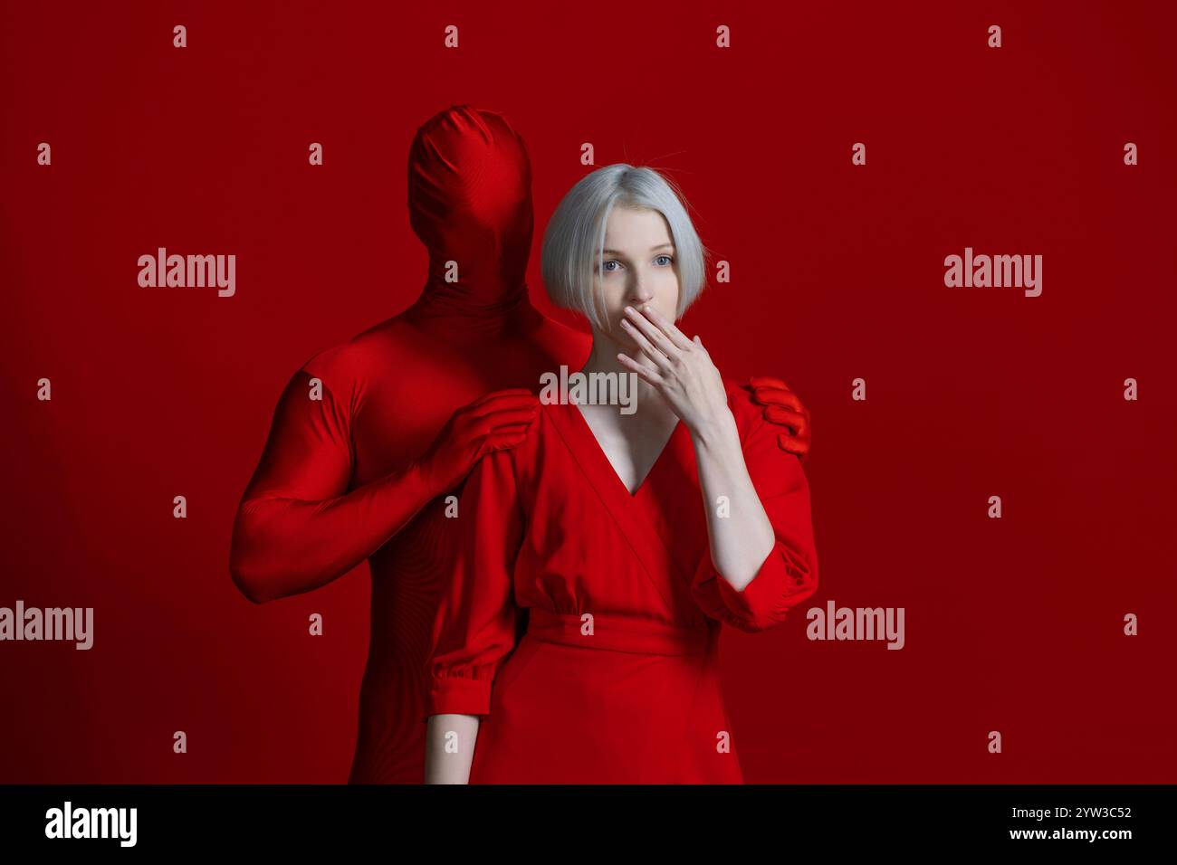 Ein Teil von mir, individuell oder von außen auferlegt. Etwas von innen und etwas von außen als Teil einer einzigen Persönlichkeit, eines Konzepts. Eine Frau in einem roten Kleid und eine gesichtslose Figur in Rot berührt sie mit seinen Händen, Foto auf Rot Stockfoto