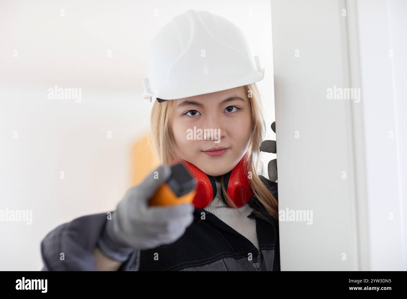 Eine junge Ingenieurin mit weißem Helm und Gehörschutz hält ein Walkie-Talkie aus. Stockfoto