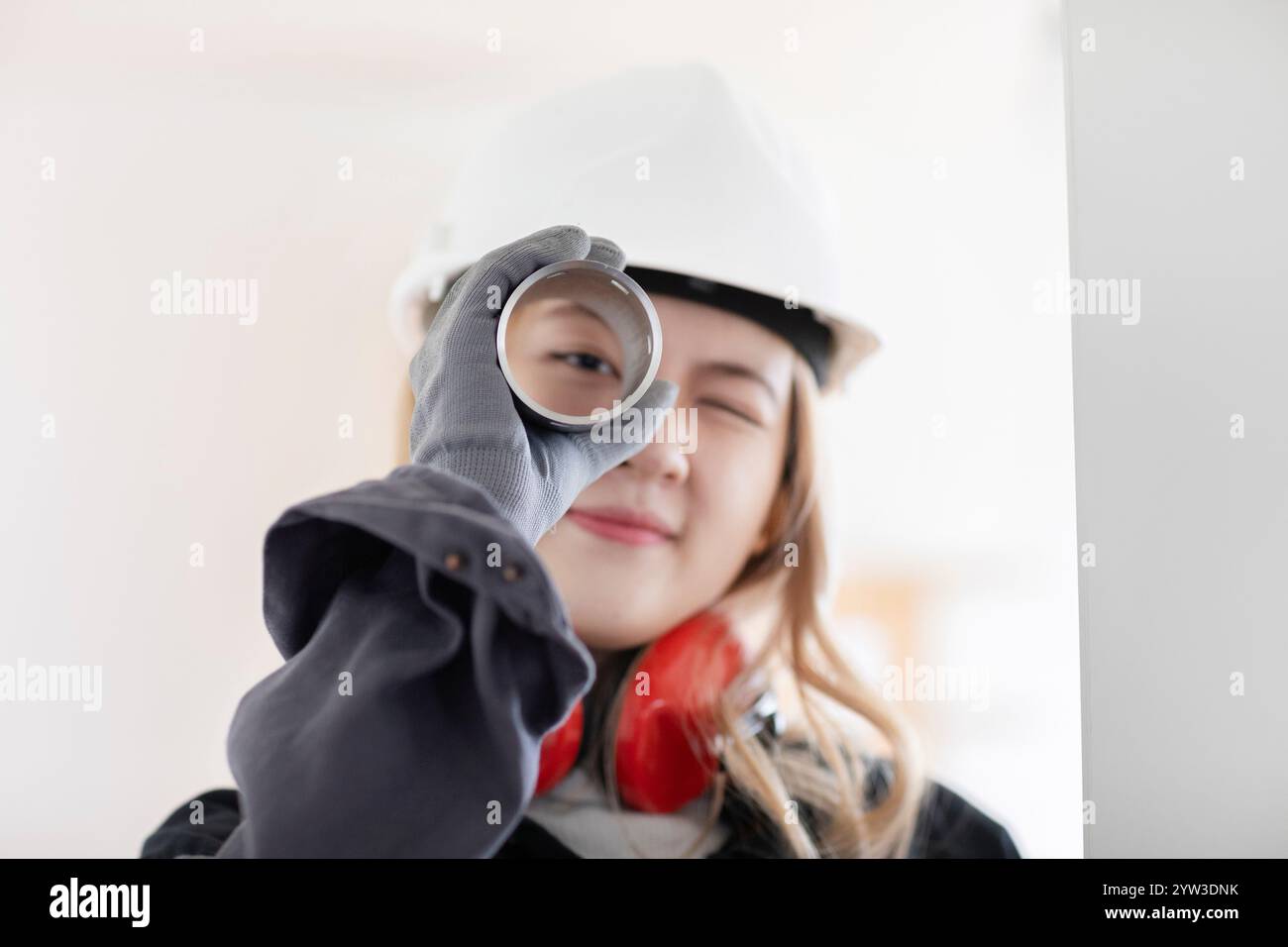 Lächelnde Ingenieurin, die einen Schutzhelm trägt und einen aufgerollten Plan durchschaut. Stockfoto