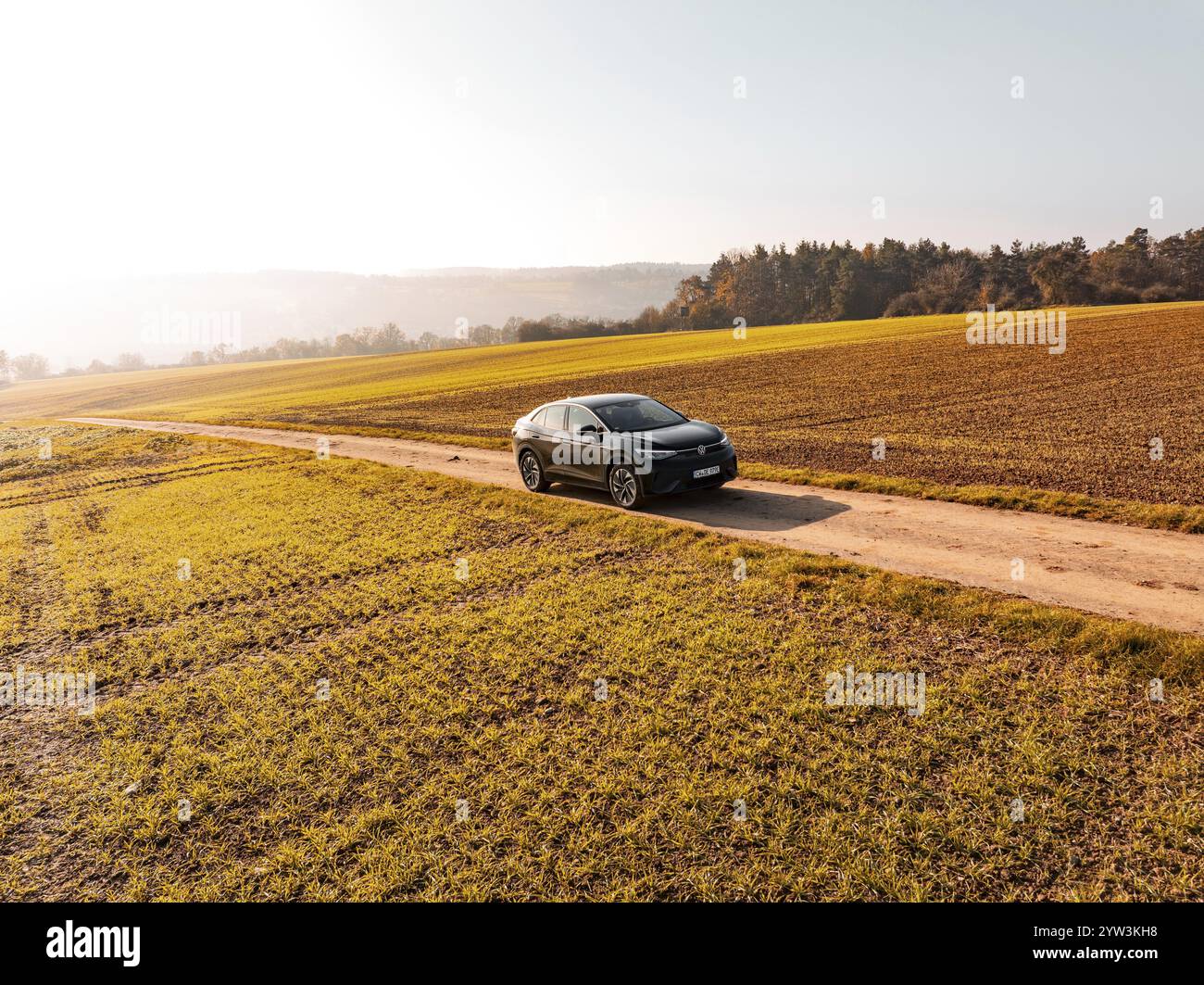 Ein schwarzes Auto auf einer unbefestigten Straße inmitten goldener Herbstfelder im Sonnenlicht, Elektroauto VW ID5, Deer Carsharing, Gechingen, Schwarzwald, Deutschland Stockfoto