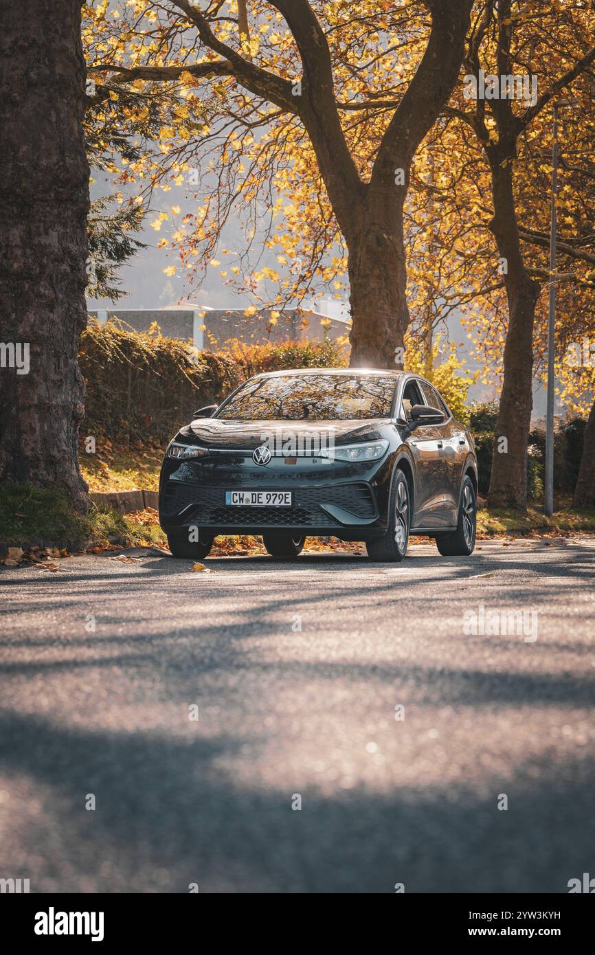 Auto auf Herbststraße flankiert von Sonne und Bäumen, Elektroauto VW ID5, Deer Carsharing, Gechingen, Schwarzwald, Deutschland, Europa Stockfoto