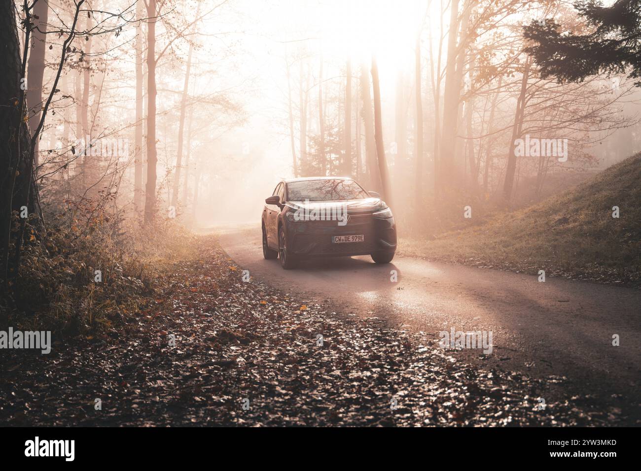 Ein Auto auf einer nebeligen Straße im Herbstwald mit goldenem Sonnenlicht am Morgen, Elektroauto VW ID5, Deer Carsharing, Gechingen, Schwarzwald, Deutschland, Eu Stockfoto